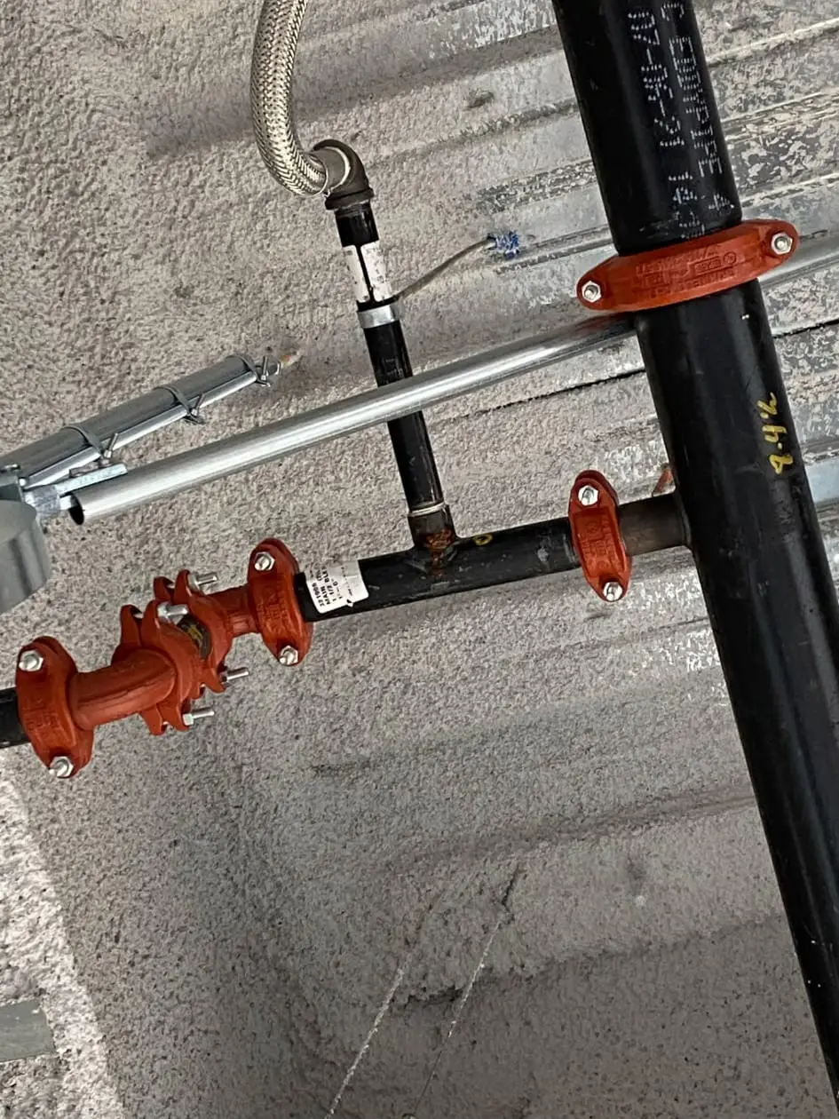 Orange grooved couplings on fire sprinkler branch piping beneath a concrete deck.